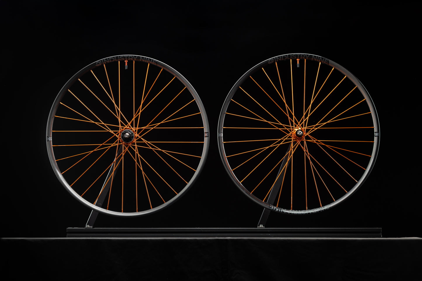 Two bicycle wheels with orange spokes on a black background
