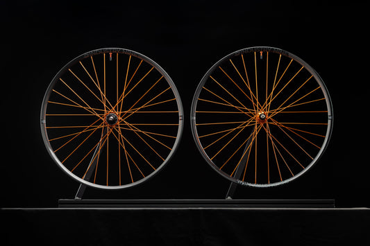 Two bicycle wheels with orange spokes on a black background