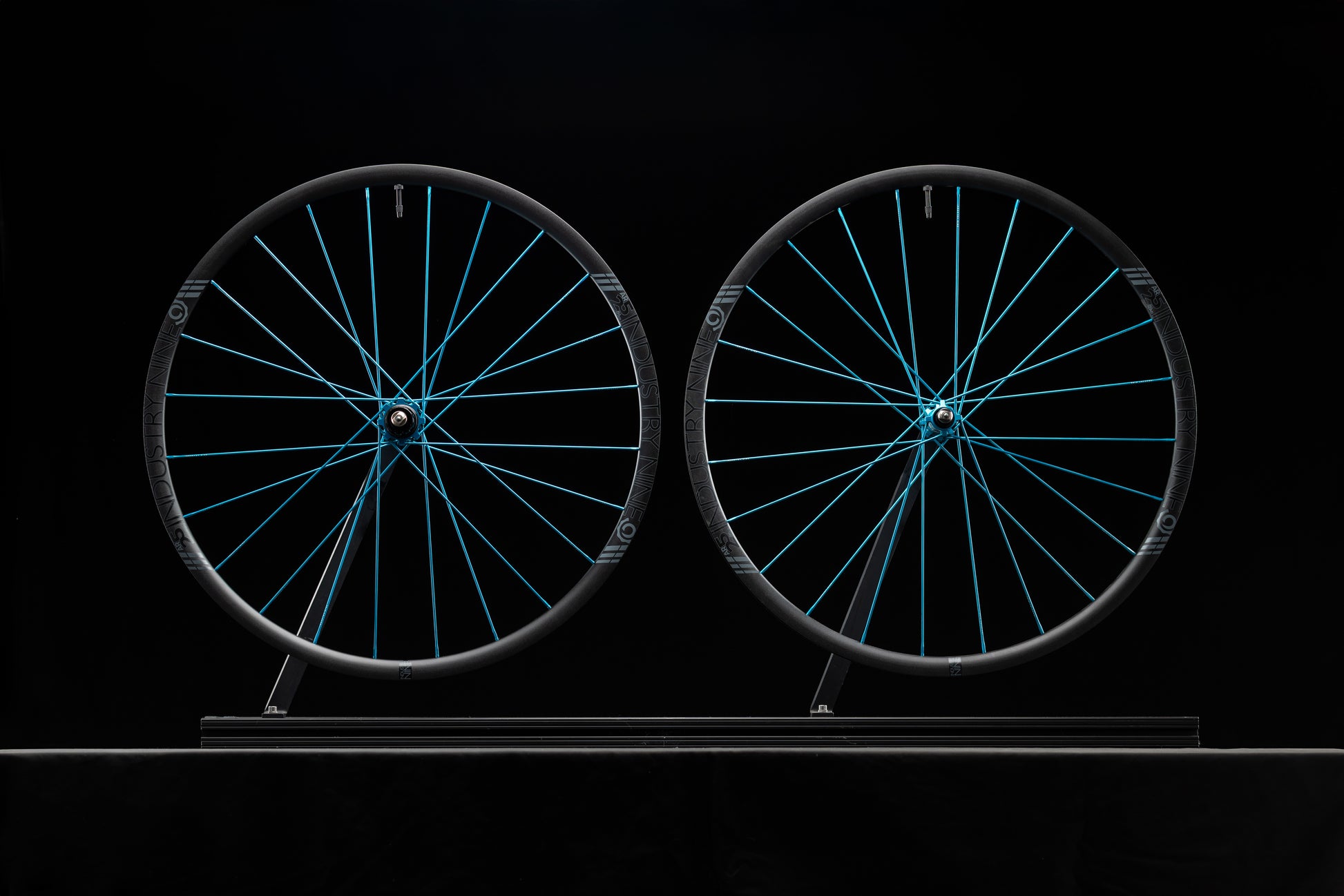 Two bicycle wheels with turquoise spokes on a black background