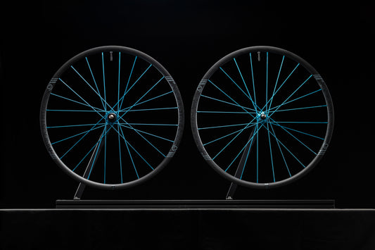 Two bicycle wheels with turquoise spokes on a black background