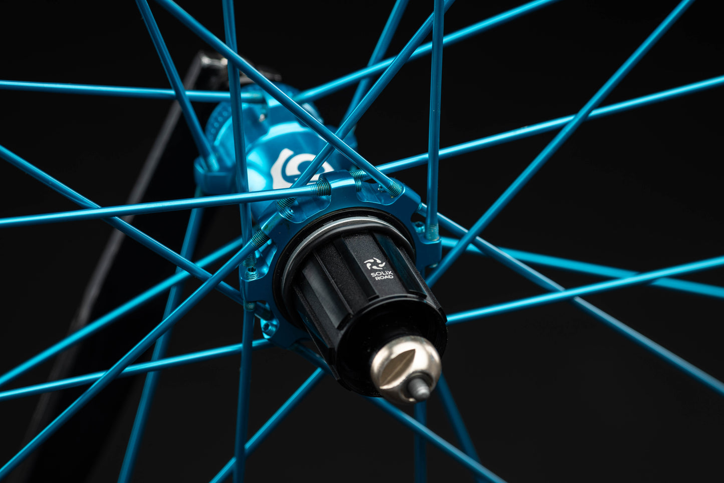 Close-up of a bicycle wheel hub with turquoise spokes on a black background