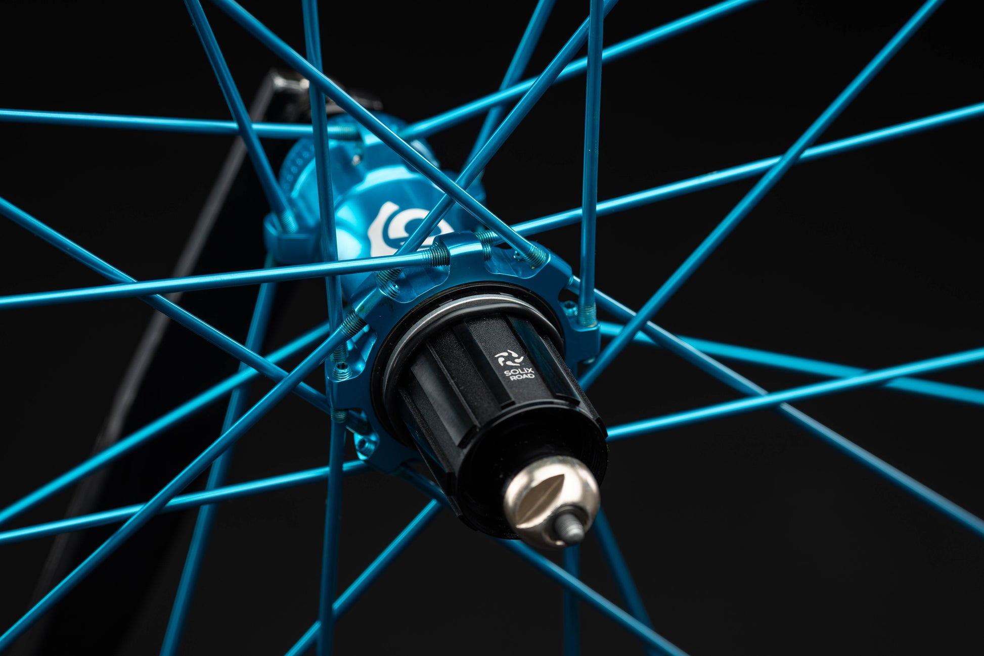 Close-up of a bicycle wheel hub with turquoise spokes on a black background