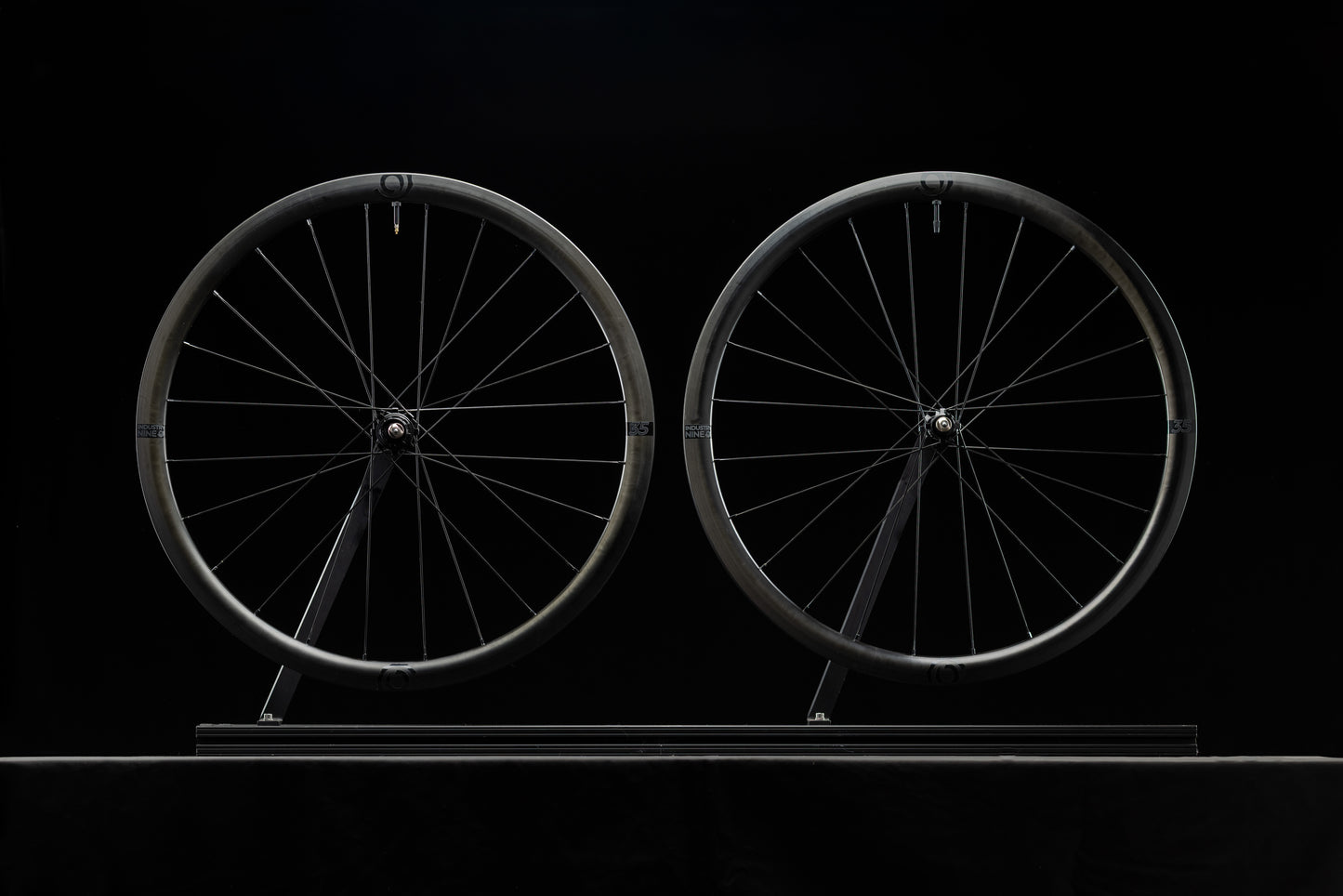 Two bicycle wheels on a stand against a black background