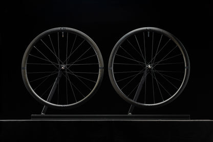 Two bicycle wheels on a stand against a black background