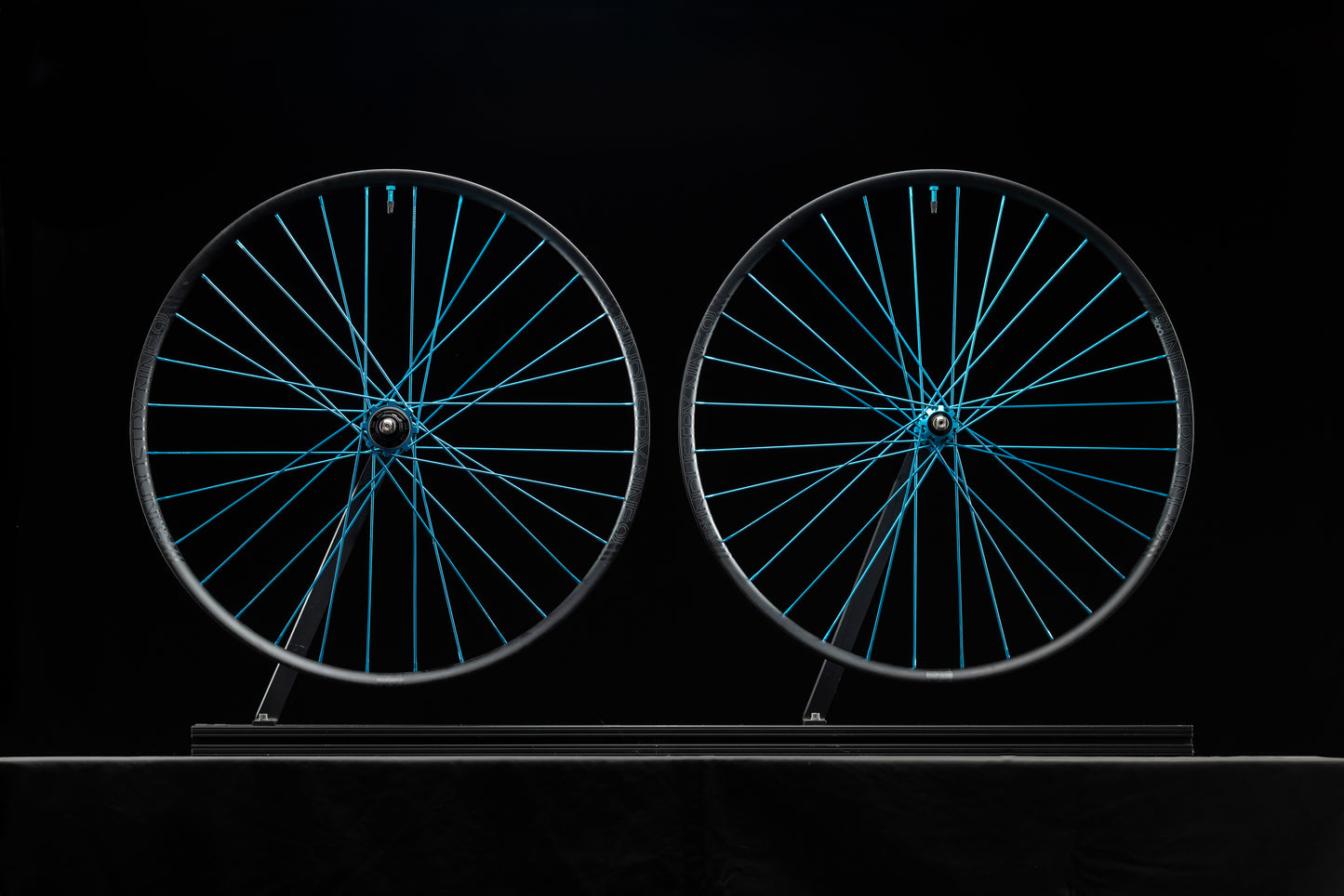 Two bicycle wheels with turquoise spokes on a black background