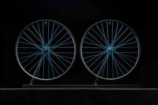 Two bicycle wheels with turquoise spokes on a black background
