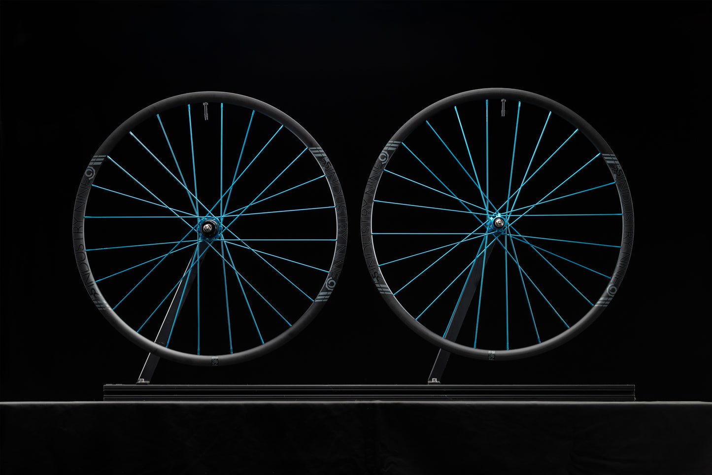 Two bicycle wheels with turquoise spokes on a black background