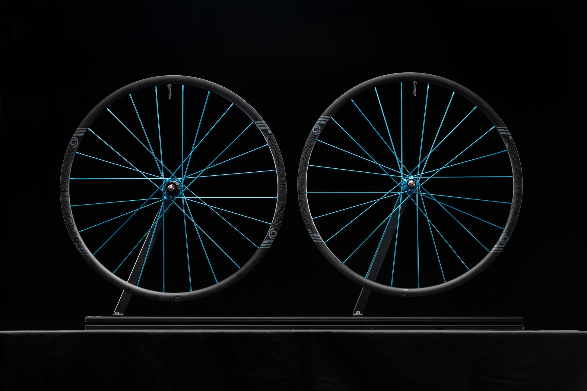 Two bicycle wheels with turquoise spokes on a black background