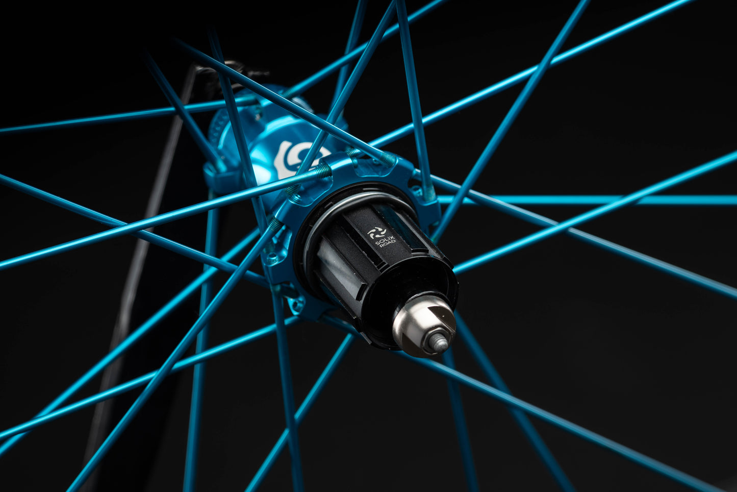 Close-up of a bicycle hub with turquoise spokes on a black background